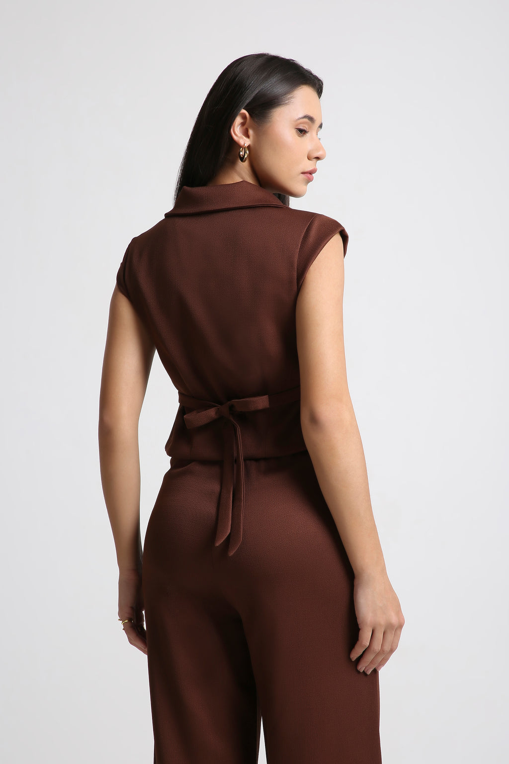 Brown sleeveless blazer top with tie back and matching high waist wide leg trousers modeled in a studio by a female fashion model from Muzera for women's co ord sets and business casual outfits.